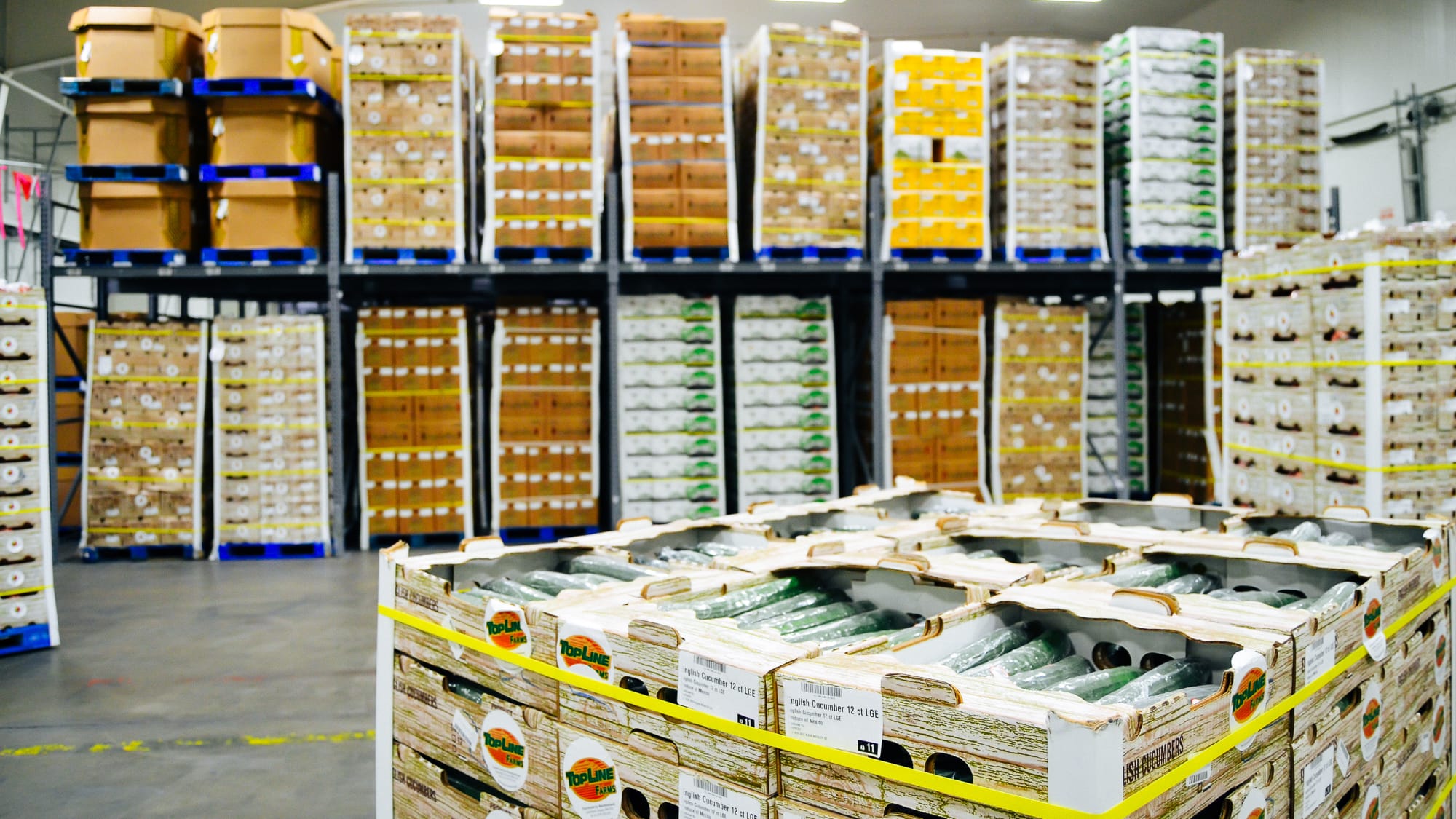 Fresh produce crates staged on a warehouse floor with high pallet racking of commodities behind